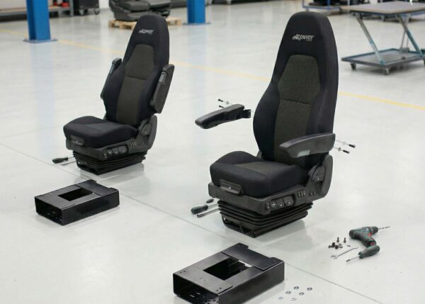Close-up of a semi truck seat with adjustable armrests, fabric upholstery, and suspension base during installation